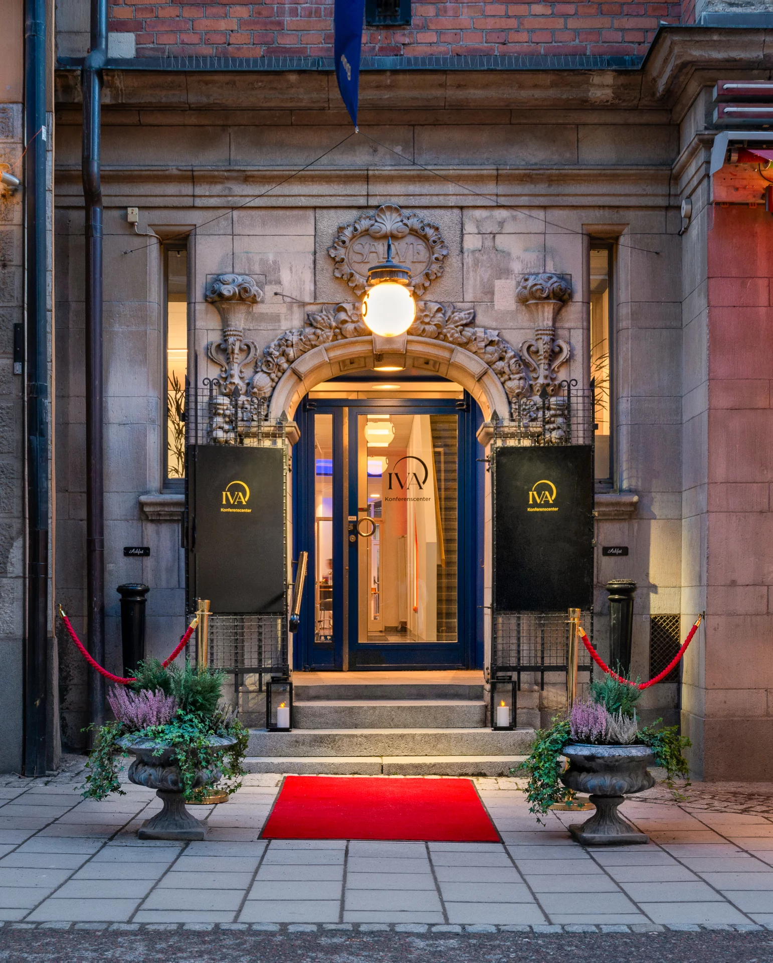 Entrén till IVA Konferenscenter med stenportal, inskriptionen SALVE, röd matta i trappan och skyltar i guld.